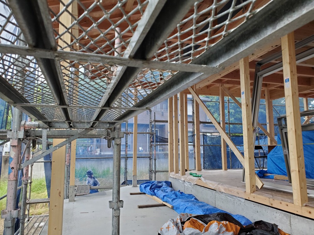 奈良県内で新築中の木造二階建て住宅現場の様子。構造材（柱・梁）が組み上がり、仮設足場が設置された棟上げ直後の建築現場。リビングからつながる軒下テラススペースを想定した設計で、光や風、自然とのつながりを意識した開放的な間取りが特徴。やまぐち建築設計室による設計監理のもと、家づくりのリアルな過程を体感できる現場風景。
