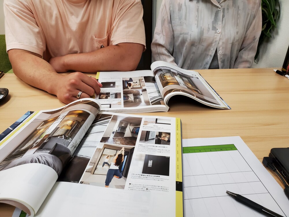 やまぐち建築設計室にて平屋住宅の新築設計を打ち合わせ中のご夫婦。建材カタログを見ながら、奈良県中南和エリアでの土地探しからスタートしたホテルライクな住まいの計画を進行中。暮らしに寄り添う間取りとインテリアの方向性を建築家とともに検討している様子。