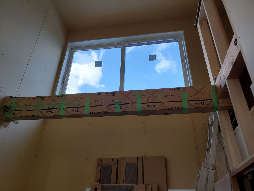 和モダン住宅の吹き抜けに設けられた高窓と、養生された見せ梁の施工状態。自然光の取り込みと構造美を調和させた設計意図が見える。