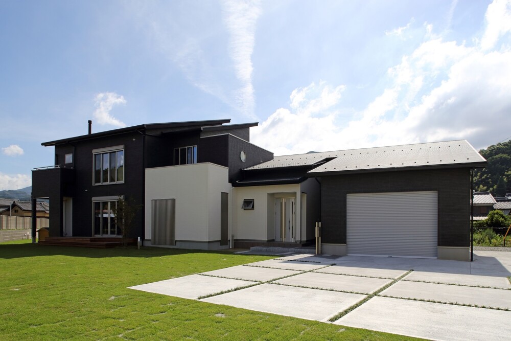 奈良県の建築家設計による和モダンの注文住宅。黒と白の外壁を組み合わせたシンプルモダンな邸宅で、広い庭と駐車スペースを備える。ウッドデッキや中庭とつながる設計により、週末住宅・セカンドハウスとしても魅力的な暮らしを提案