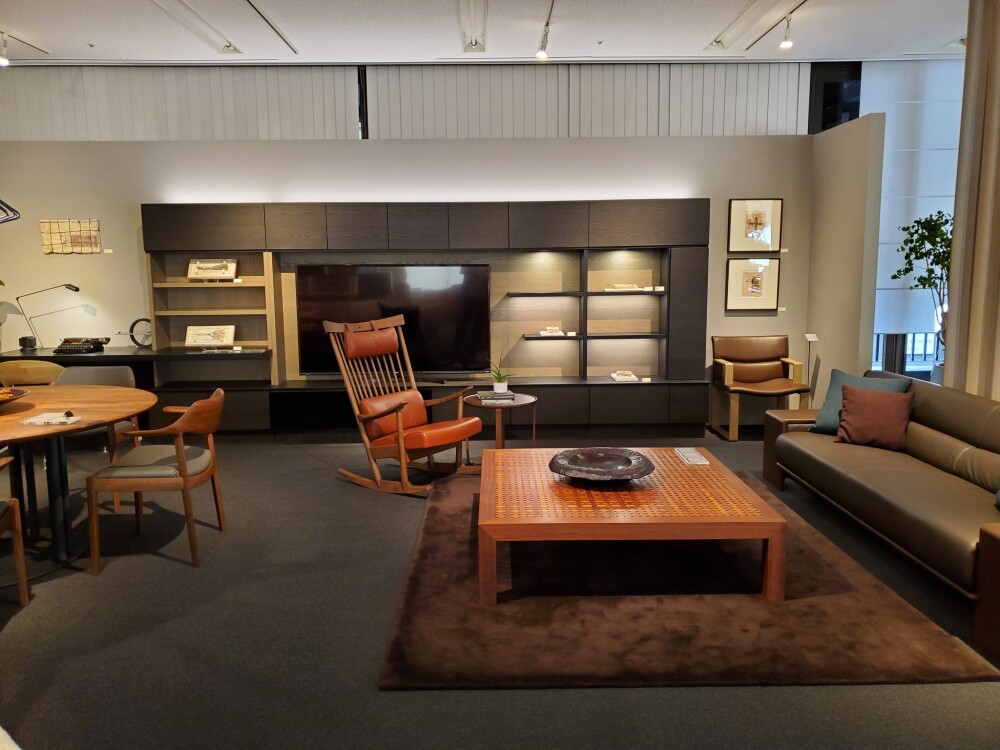 カンディハウス大阪ショールームのリビング展示。無垢フローリングとカーブソファ、間接光が織りなすジャパンディな設え。外の緑と調和し、奈良の暮らしにも馴染む建築家視点の上質空間。