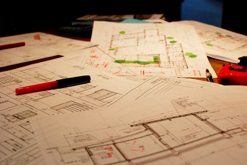 注文住宅の間取り設計に用いる建築模型と各種図面が広げられ、動線計画・ゾーニング・採光などを検討している様子を写した写真。計算機やスケール、筆記具とともに、生活動線・家事動線・収納計画を総合的に読み解きながら、未来の暮らしをデザインするプロの建築設計プロセスを表現している。奈良の建築家・やまぐち建築設計室の丁寧な家づくりを象徴するイメージ。