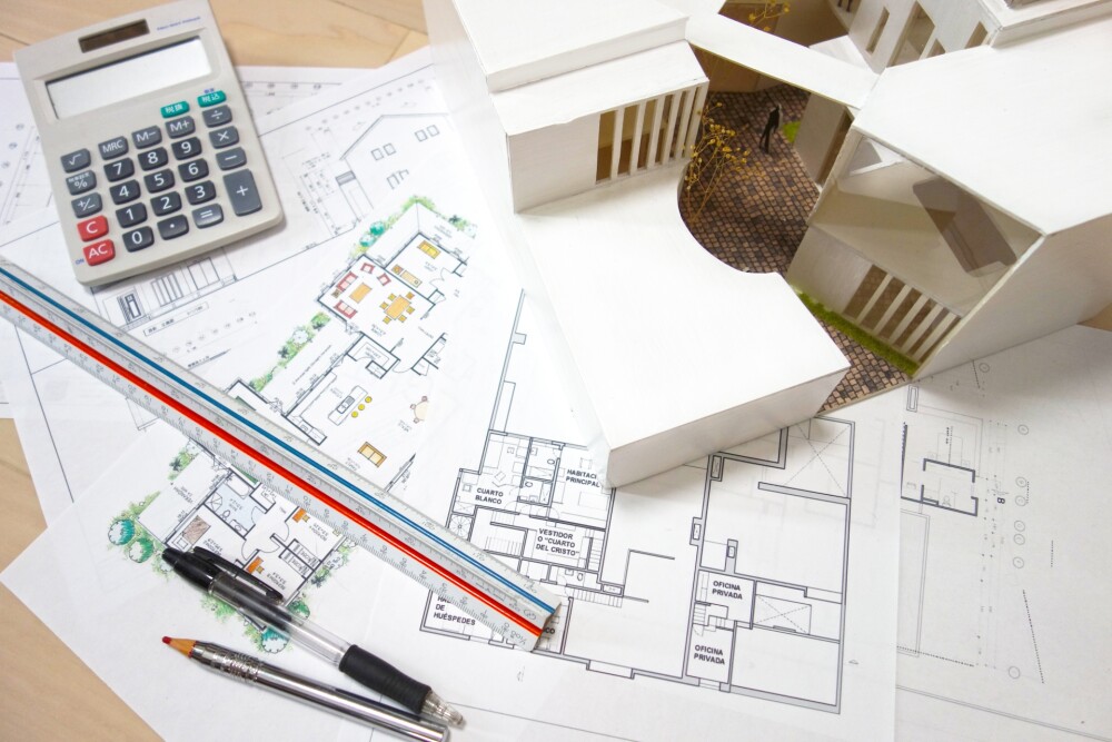 家事動線と収納計画を丁寧に設計するための、建築模型・間取り図・スケール・電卓が並ぶ設計デスクの様子。やまぐち建築設計室が、暮らしやすい和モダン住宅のために行う詳細な間取り検討と、家事が軽くなる動線計画のプロセスを示すイメージ。