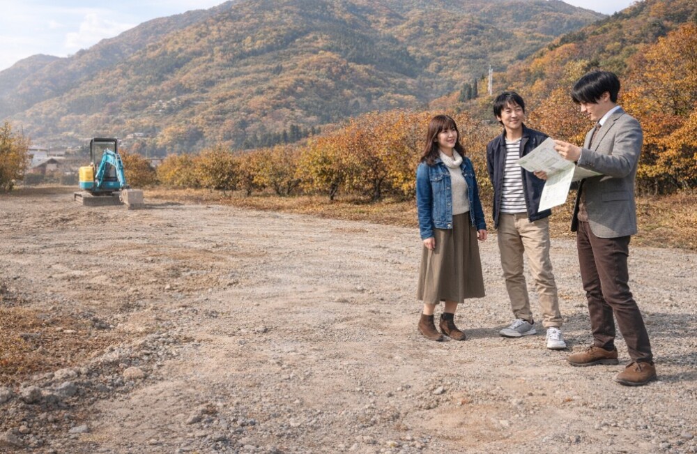 奈良県の山間部にある土地で、移住を検討するご夫婦が建築家とともに現地を確認し、敷地条件や将来の暮らしを話し合っている秋の風景