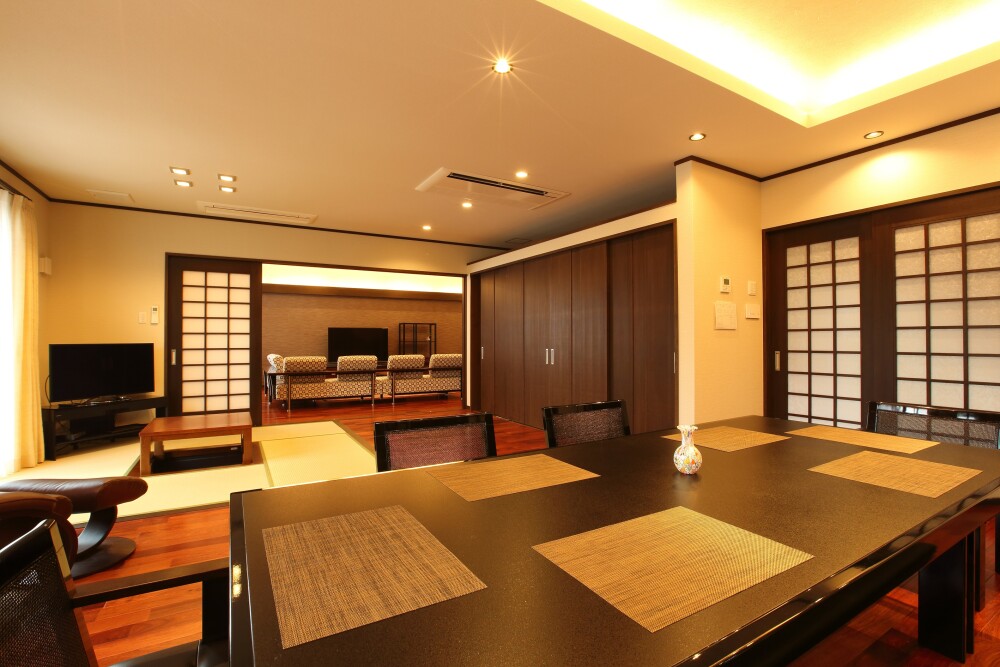 和モダン住宅のLDK空間。障子建具と間接照明を組み合わせたホテルライクなダイニングと、畳スペース・リビングが緩やかにつながる設計。光と影のバランスを整え、落ち着きと高級感を両立した建築家設計の和モダンの家。