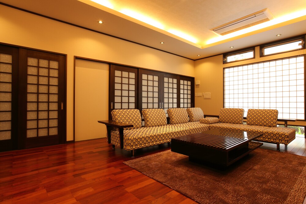 和モダン住宅の広々としたリビング空間。障子建具と折り上げ天井の間接照明が調和し、光と影のコントラストでホテルライクな落ち着きを演出する設計。木質フローリングと和の意匠を融合した、建築家が手がける高級和モダンの家。