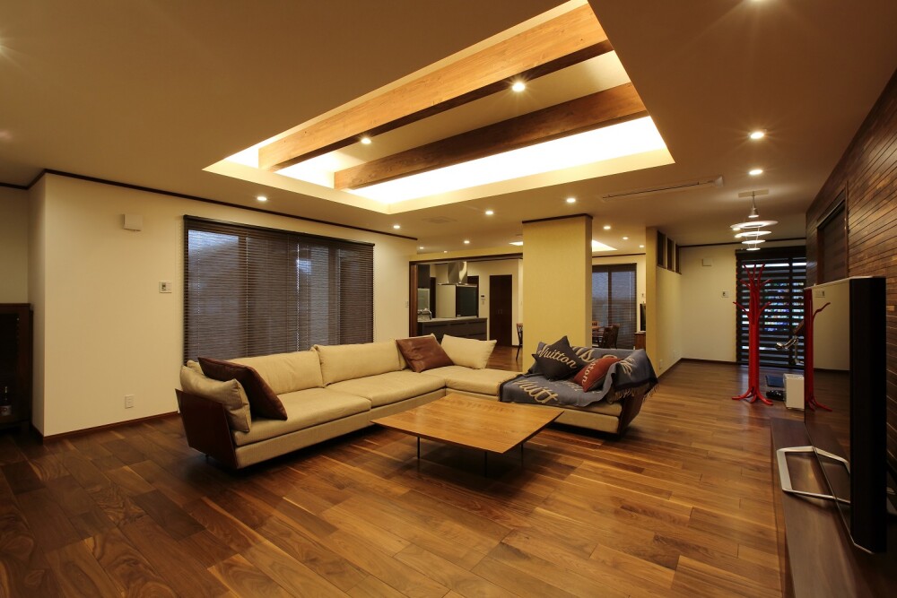 和モダン住宅の広々としたLDK空間。折り上げ天井に仕込んだ間接照明と木梁が、光と影の奥行きを生み出すホテルライクなリビング。無垢フローリングと上質な家具配置により、建築家・設計事務所が手がける高級和モダンの住まいを表現している。