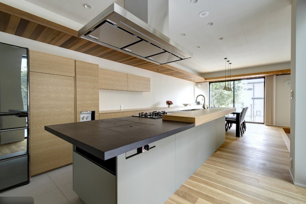 和モダンなホテルライク空間として設計されたアイランドキッチン。 グレーのキッチンと木天井を組み合わせ、背面収納と一直線の動線により、料理がしやすく気持ちが落ち着く住まい環境を実現した建築家設計のキッチン空間。