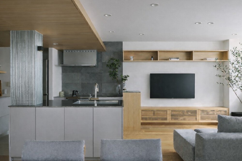 和モダン&times;ホテルライクなLDK。木目天井とグレーのアイランドキッチン、壁掛けテレビと造作の木製テレビボードを一体化し、生活感を抑えた収納設計で暮らしやすさを高めた注文住宅のインテリア。