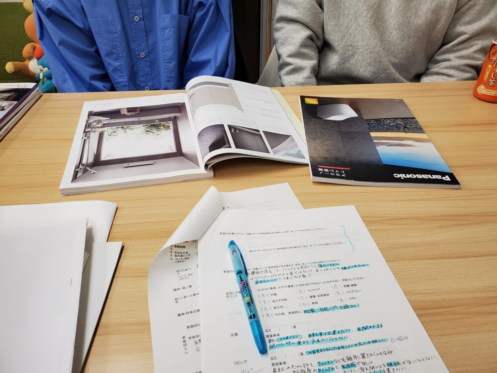 家づくりの打ち合わせ風景。建築家と住まい手がテーブルを囲み、住宅設備カタログや設計資料、暮らしのヒアリングシートを広げながら、間取りやデザインではなく「これからの暮らし方」について対話を重ねている様子。奈良県の建築設計事務所・やまぐち建築設計室による、人生に寄り添う注文住宅の設計プロセス。