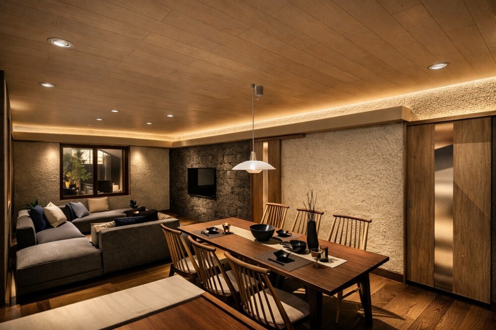 和モダンとホテルライクを融合させたLDK空間。木目天井と塗り壁に建築化照明を組み込み、間接光のグラデーションによって夜の時間をやさしく包み込む設計。ダイニングとリビングが緩やかにつながり、富裕層・パワーカップルのための癒しと静けさを重視した住宅インテリア提案。