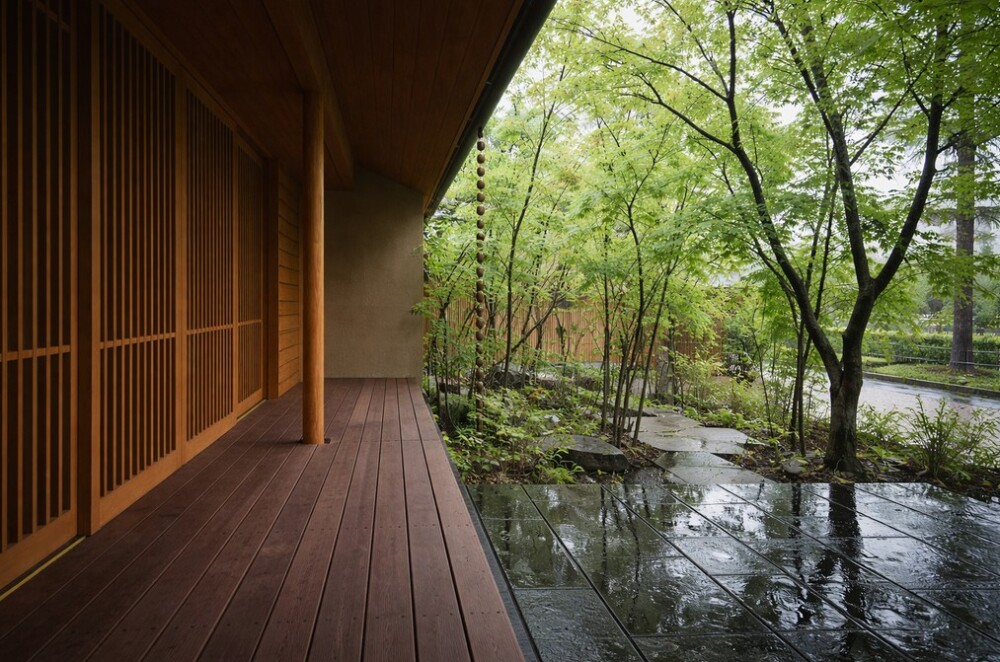 和モダン住宅の縁側と庭の情景。木格子と深い軒に守られた半屋外空間が、自然と内面の静けさをつなぎ、制約の中で人生の質を整える住まいの設計思想を表している。