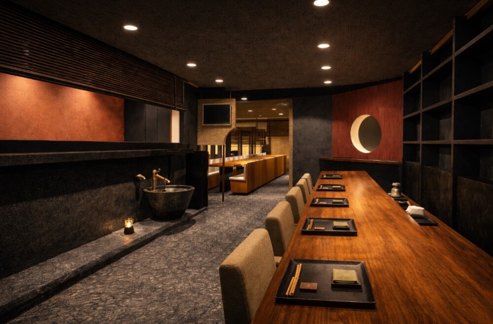 高級和食料理店のカウンター内装デザイン事例。 料理を味わう前に心がほどけることを重視し、抑制された照明計画と暗がりが生む安心感、わびさびの美意識を反映した素材構成により、五感を静かに整える和のサロンのような空間を実現。 料理人の所作を引き立てるカウンター設計と、視線と動線を緩める空間構成によって、食事体験そのものの質を高めた高付加価値な飲食店設計。 和食店・割烹・料亭などの新規出店や店舗リニューアルを検討する飲食店経営者、店舗オーナー、企業、社長、マネージャー向けの店舗デザイン提案。