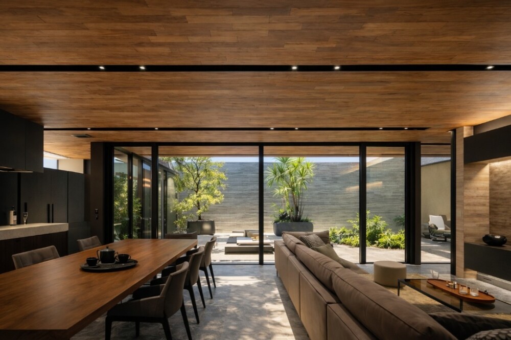 奈良の建築家設計による和モダン住宅のLDK。木質天井とホテルライクな間接照明、石調フロアが静かな品格を生み、中庭とつながる大開口が自然光と庭の緑を取り込む。人生の喜怒哀楽を受け止める住まいという建築思想を表現した注文住宅の空間デザイン。