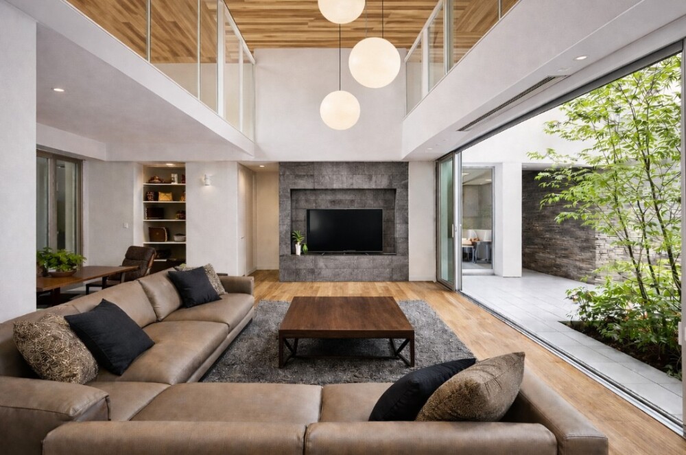 自然光を程よく取り入れる吹き抜けリビングのある注文住宅。奈良の建築家が設計したホテルライクなモダン住宅で、朝日ウッドテックのオークフローリングと木目天井の方向を揃えた空間に、ポルトローナフラウのソファとリッツウェルJKテーブルを配置。テレビ背面にはグレーのエコカラットを採用し、大開口窓から中庭の緑と自然光を取り込むことで、光と陰影を美しく整えた上質な住まい。