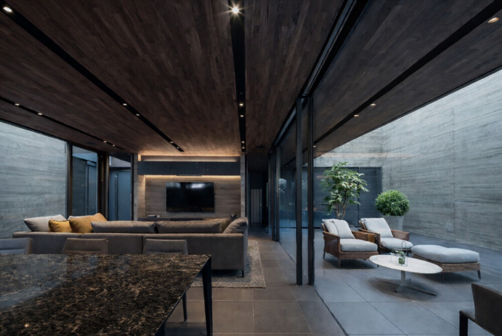 奈良の建築家による注文住宅のリビングダイニング空間。大開口サッシを通して中庭テラスと一体化したLDKで、縁側や土間テラスのような中間領域「内的外部」を取り入れた住まいの設計。木張り天井と御影石ダイニングカウンター、ホテルライクな照明計画が落ち着いた空間をつくり、テラスにはポルトローナ・フラウの屋外家具とパキラ・ポトスの観葉植物を配置した建築家住宅の空間デザイン。