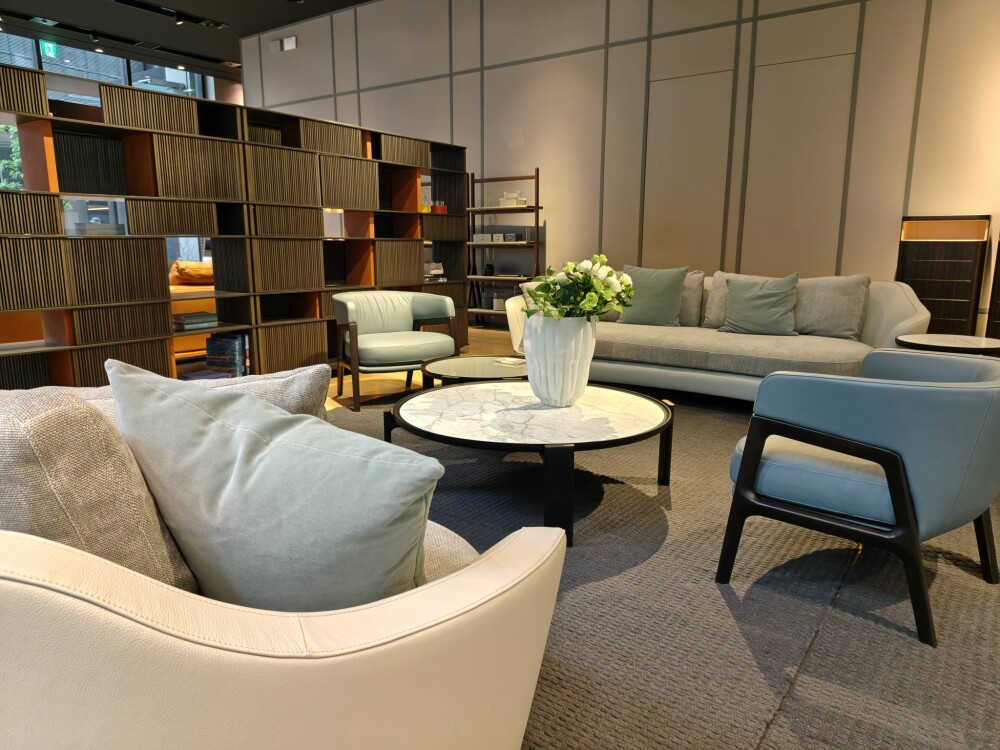 ポルトローナ・フラウ大阪ショールームのゾーニング設計。格子状のシェルフで空間を緩やかに仕切り、グレートーンのソファとラウンジチェアを配置。光と陰影、素材の質感を活かした静かなラグジュアリー空間のインテリアコーディネート事例。