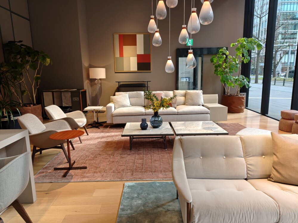 ポルトローナ・フラウ大阪ショールームのラウンジ空間。ベージュのレザーソファと大理石テーブル、ガラスペンダント照明が調和し、自然光と暖色照明が重なり合うホテルライクなリビングインテリア。家具と空間設計が一体となった上質な暮らしの提案。