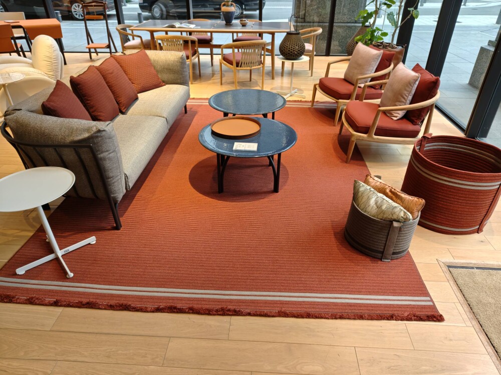 ポルトローナ・フラウ大阪ショールームのインテリアコーディネート事例。テラコッタカラーのラグとグレーファブリックソファ、ラウンジチェアが円形テーブルを中心に配置され、動線と居場所を整えた落ち着きのあるリビング空間デザイン。