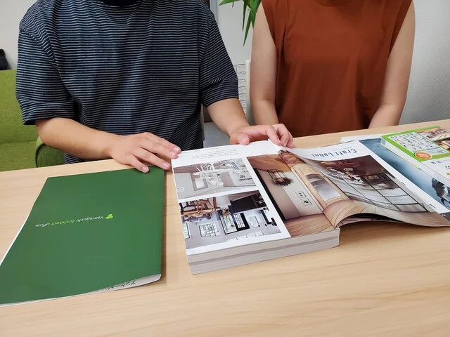 奈良県で家づくりを検討するご夫婦が、施工事例カタログやインテリア資料を見ながら間取りや暮らし方について話し合っている様子。新築注文住宅・建て替え・リノベーションに向けて、自分たちの価値観や生活動線を整理する住まい相談の一場面。