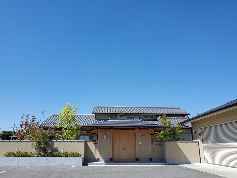 奈良県の住宅地に建つ、数寄屋の趣を取り入れた高級和風住宅・和モダン住宅の外観。瓦屋根と深い軒、木製門扉と塗り壁、整えられた植栽により、外からの視線をやわらかく遮りながら内に静けさを生み出す設計。建築家による注文住宅で、旅館のような落ち着きと暮らしの質を重視した住まい。