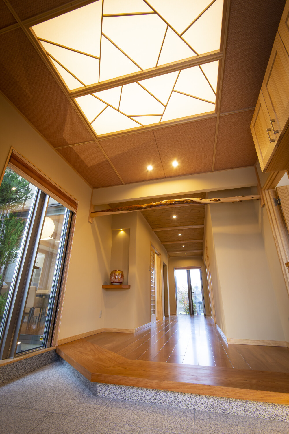 奈良の建築家が設計した数寄屋の趣を持つ和風住宅・和モダン住宅の玄関内観。間接照明を組み込んだ天井と木の梁、無垢材の床、庭に抜ける視線設計により、光と陰影が美しく広がる空間。来客を穏やかに迎え入れ、暮らしの質と時間の豊かさを高める高級注文住宅。