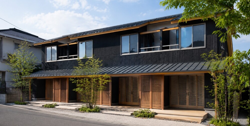 和モダン木造アパート・賃貸住宅の外観完成イメージ。 奈良の建築家・やまぐち建築設計室が提案する、数寄屋思想と現代的デザインを融合した収益物件計画。黒を基調とした落ち着きある外観に、木格子・深い軒・木の質感を丁寧に取り込み、旅館のような静けさとホテルライクな上質感を演出。 単なるローコスト木造アパートではなく、“住みたくなる空気感”を大切にした和モダン賃貸住宅として、長期的な入居率・空室対策・資産価値を見据えた設計提案。 共用部には余白と陰影を意識したアプローチ空間を設け、暮らしやすさ・居心地・プライバシー性にも配慮。奈良・大阪・関西エリアで、土地活用、木造アパート建築、デザイナーズ賃貸住宅、和モダンの収益物件を検討中の方へ向けた建築家による空間提案。