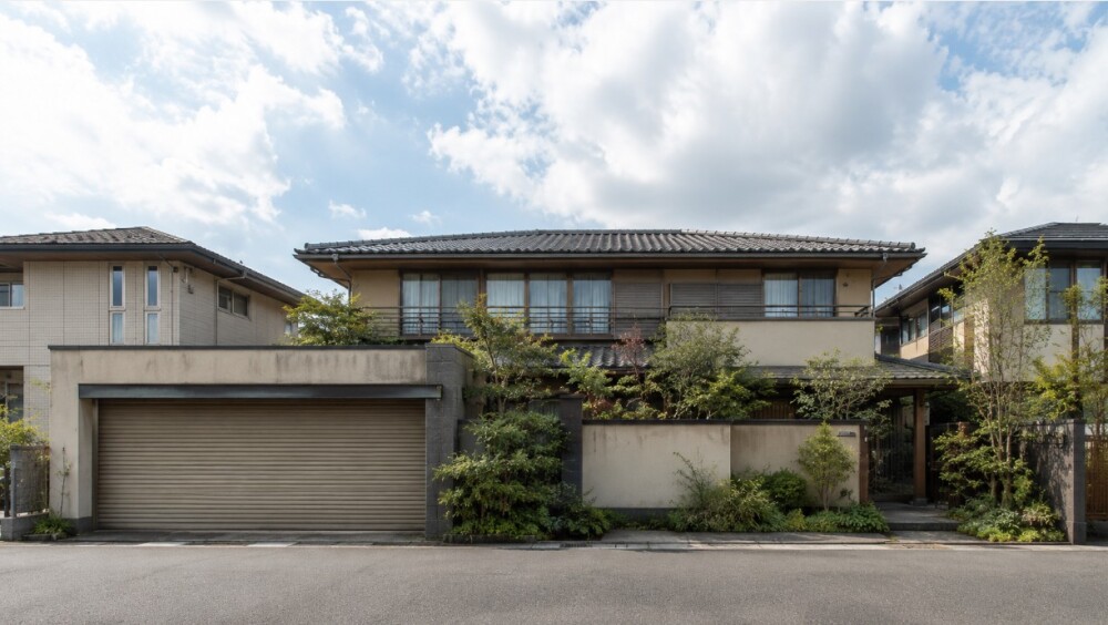 奈良県の住宅地に建つ平成3年築を想定した和風中古住宅。瓦屋根、深い軒、ビルトインガレージ、塀と植栽のある二階建て外観で、購入前の内覧とリフォーム検討を表したイメージ。