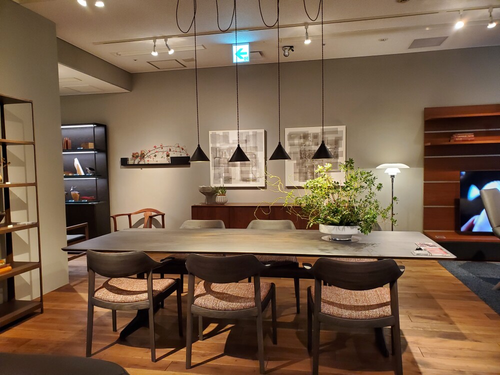 家具ショールームに展示された大きなダイニングテーブルとベンチ、和紙調の大型ペンダント照明、収納家具を組み合わせたインテリア。家具の幅や奥行き、天井高、照明との距離を確認し、住まいに合う家具サイズを検討する展示空間