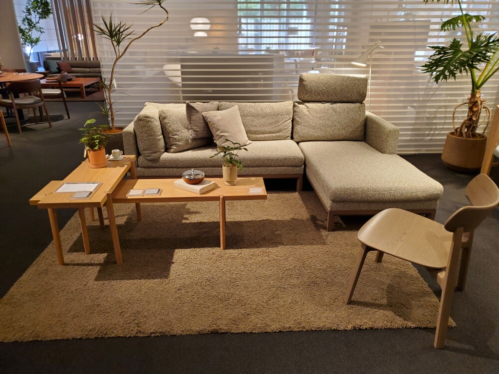 カンディハウスのショールームに展示されたカウチソファと木製センターテーブル、ラグを組み合わせたリビング空間。ソファの幅、奥行き、背もたれの高さ、周囲の通路や余白を確認し、家具選びで後悔しないレイアウトを考える参考事例