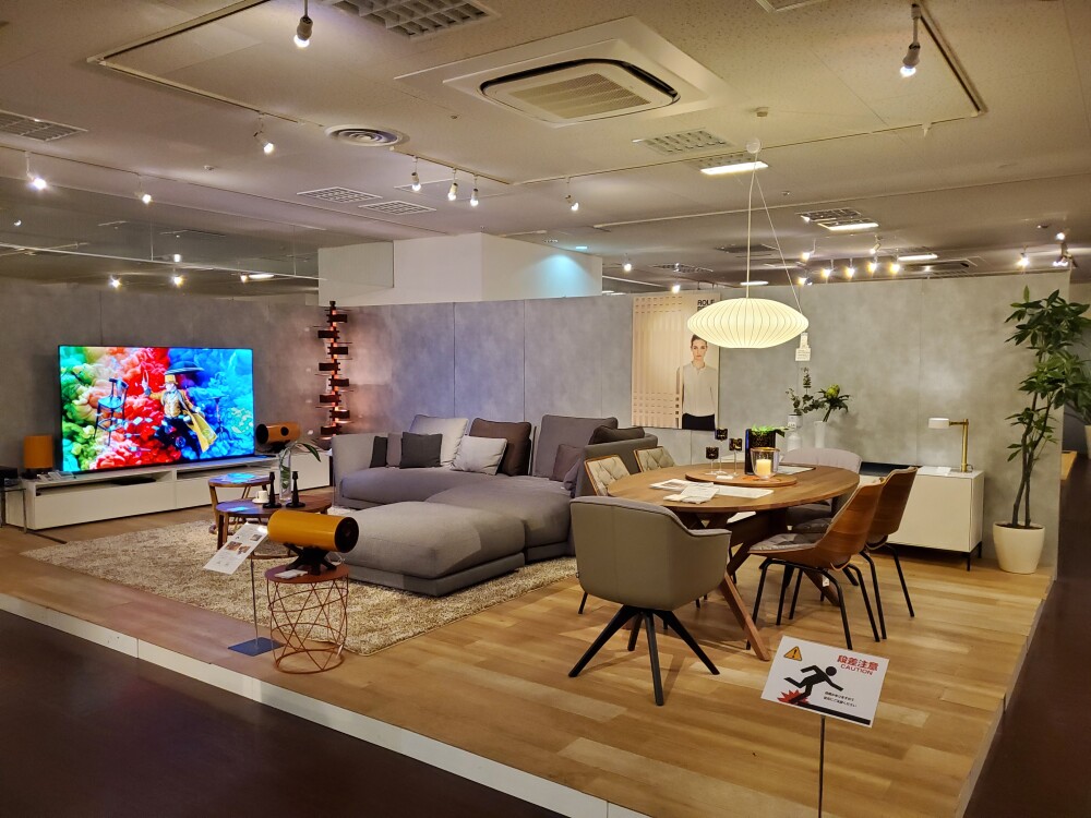 YAMADA×IDC大塚家具大阪南港ショールームに展示された大型カウチソファとダイニングテーブル、チェア、照明を組み合わせたLDK空間。ソファの幅や奥行き、家具同士の距離、生活動線、天井高とのバランスを確認し、自宅で圧迫感の出にくい家具レイアウトを考える参考事例