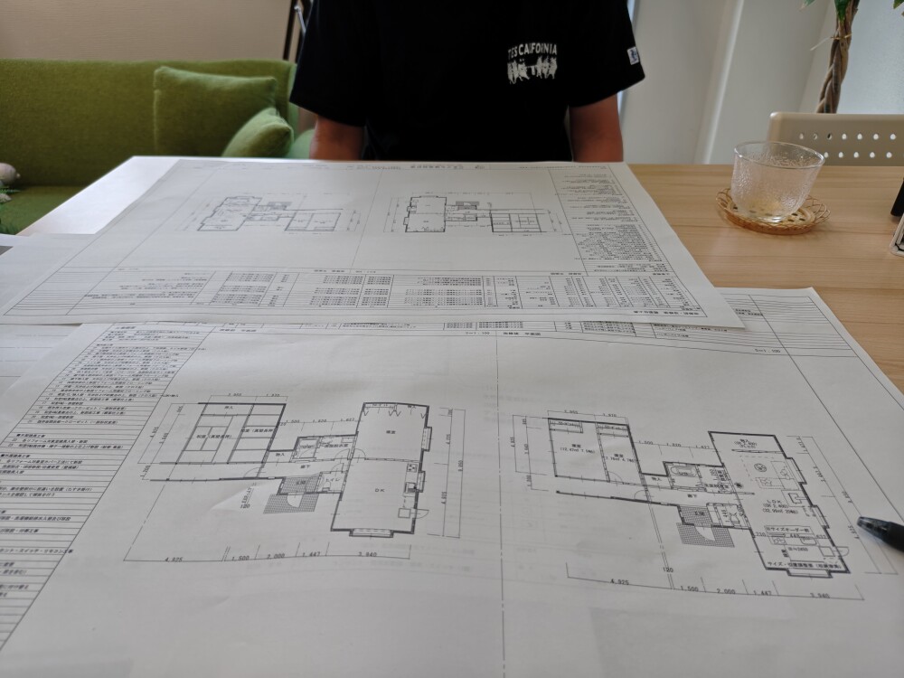 奈良県橿原市のやまぐち建築設計室で、住まい手のご主人と住宅リノベーションの図面を広げて打ち合わせ。既存の寝室・クローゼット・DKを見直し、アイランドキッチンと薪ストーブを備えた、夫婦二人のための開放的なLDKへの間取り変更を検討している様子。
