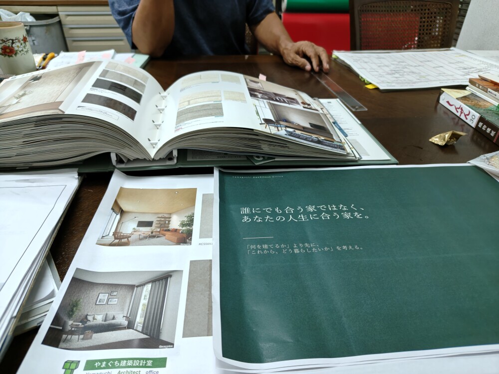奈良県のリフォーム・リノベーション住宅で、住まい手のご自宅にて壁紙・クロスの色や質感を検討する打ち合わせ風景。木製テーブルに壁紙の見本帳やインテリア資料を広げ、床材・家具・照明との調和や、これからの暮らしに合う室内空間を考える。やまぐち建築設計室によるインテリアコーディネートの一場面。