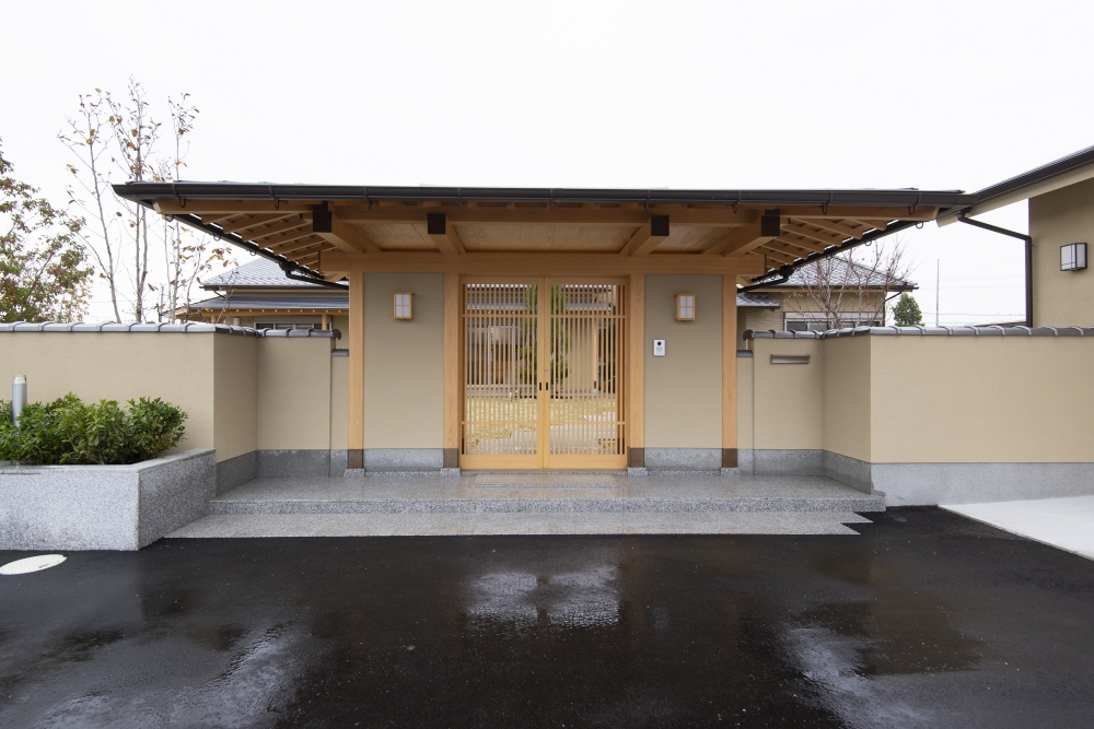奈良県のやまぐち建築設計室が設計した数寄屋風和モダン住宅の門構え外観（雨天時）。木製格子の門扉と深い軒、土塀による外構が落ち着きある迎えの空間を形成。濡れた路面に映る建築と陰影が美しく、素材の質感と静けさを際立たせる高級和風住宅の設計事例。和モダン・数寄屋住宅の上質なエントランスデザイン。