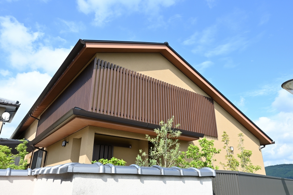 奈良県の和モダン注文住宅の外観。切妻屋根と深い軒、木格子のファサードが特徴的な住まいで、外壁の落ち着いた色調と植栽が調和。外からの視線をやわらかく遮りながら、光と風を取り込む設計により、静けさと上質な暮らしを実現した住宅事例。