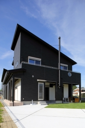 黒を基調とした外壁が印象的な和モダン住宅の外観。大きく張り出した屋根と水平ラインを強調したファサードが、重厚感と洗練された佇まいを演出。パントリーから直接アクセスできる勝手口を設け、家事動線と外部動線を効率化した設計。芝生の庭とフラットに続く外構計画により、暮らしやすさとデザイン性を両立したホテルライクな住まい。