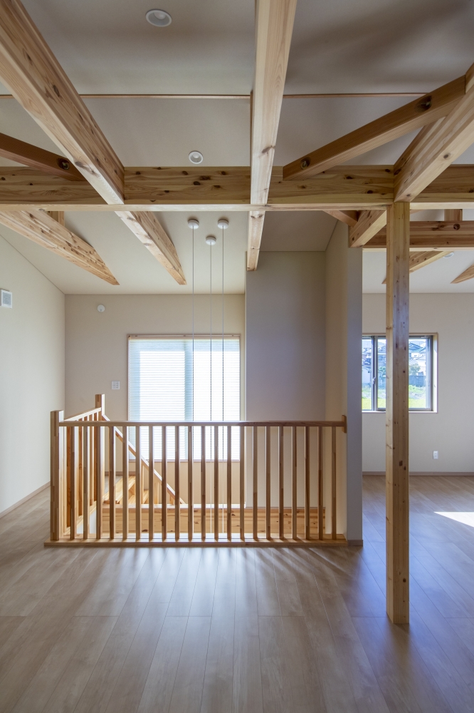 無垢材の梁と吹抜け空間が印象的な、和モダン住宅の二階フリールーム。木組みの構造美をあえて見せることで、空間全体にリズムと温もりを与え、自然光がやわらかく広がる開放的な住空間を演出している。吹抜けを介して一階LDKとゆるやかにつながり、家族の気配や光、空気感を共有できる設計。二階ホールを単なる通路ではなく、ワークスペースや読書、趣味の時間を楽しめる多目的な“余白空間”として計画し、暮らし方に柔軟性を持たせている。和モダンの家・吹抜けリビング・フリールームのある家・高級注文住宅・木の家・デザイナーズ住宅を求める方に向けた建築事例。