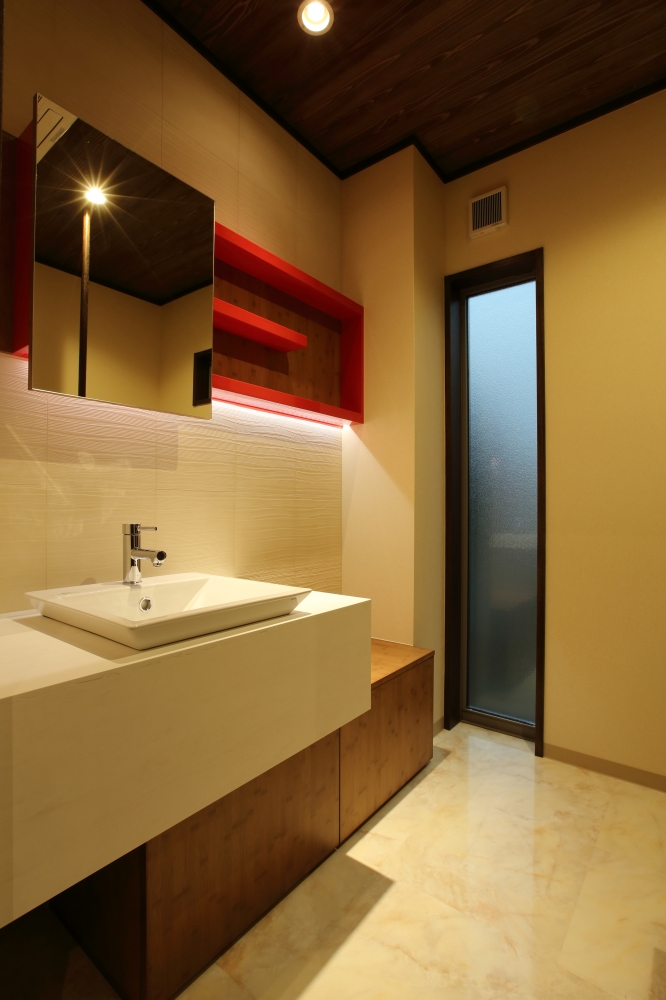 奈良の注文住宅における一階トイレ手洗いスペースの設計事例。造作洗面カウンターと間接照明を組み合わせ、ホテルライクで上質な空間を実現。木天井とアクセントカラーの収納棚が空間に奥行きを与え、機能性とデザイン性を兼ね備えた和モダン住宅の手洗い空間。