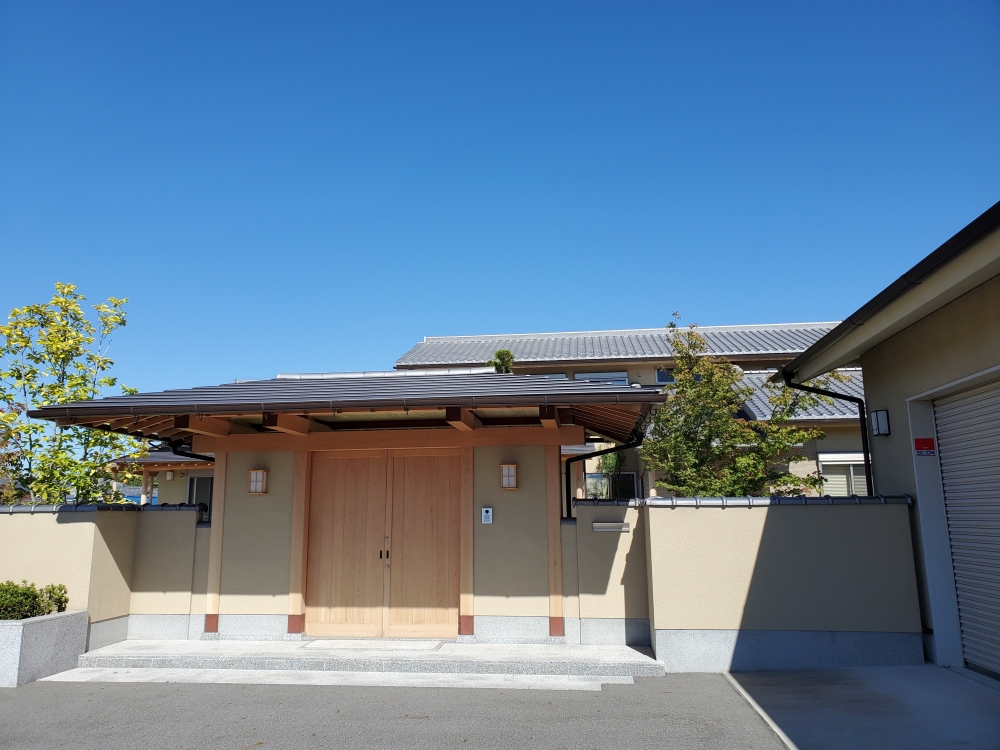 奈良県のやまぐち建築設計室が設計した数寄屋風和モダン住宅の門構え外観。木製の両開き門扉と深い軒、土塀による外構が上質なプライバシー空間を形成。瓦屋根と陰影の美しさ、行灯風照明が迎えの空間に落ち着きを与える高級注文住宅の設計事例。和風住宅・和モダン住宅における品格あるエントランスデザイン。