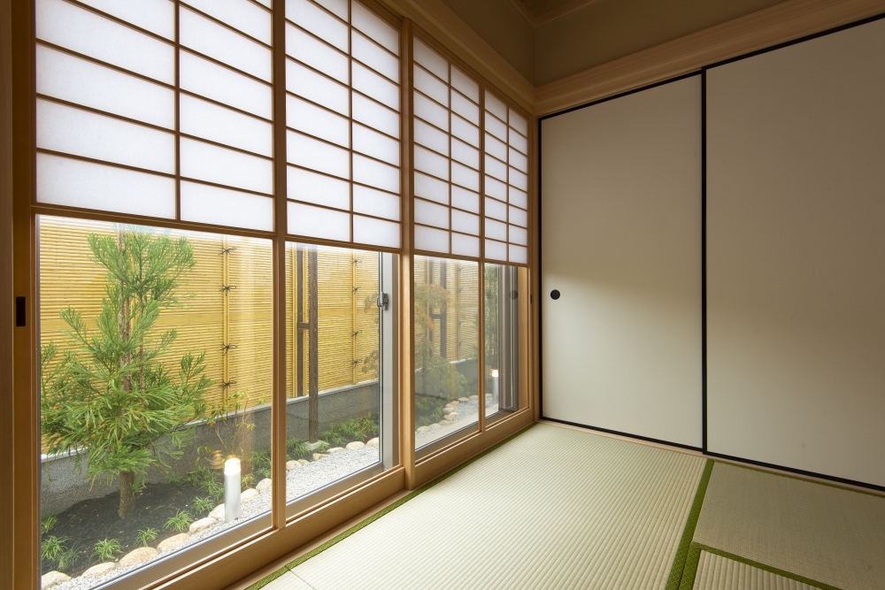 奈良県のやまぐち建築設計室が設計した数寄屋風和モダン住宅の和室と坪庭の関係性を捉えた空間。障子越しにやわらかな自然光を取り込み、畳の間と外部の植栽・竹垣が連続する設計。内と外をゆるやかにつなぐ大開口窓により、プライバシーを確保しながらも視線の抜けと静けさを生み出す高級注文住宅の事例。和風住宅・和モダン住宅・坪庭のある家の設計実例。