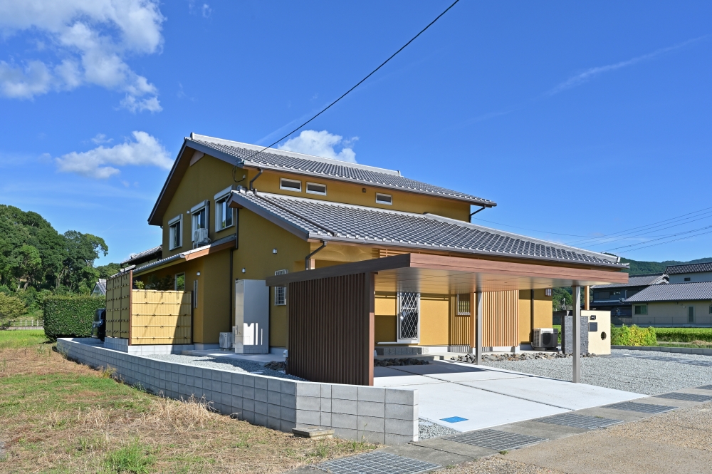 奈良県の自然風景に美しく溶け込む、和モダン住宅の外観デザイン。瓦葺きの切妻屋根と土壁調の外壁、木格子を組み合わせた数寄屋風の佇まいが、旅館のような落ち着きとホテルライクな上質感を演出。深い軒と水平ラインを整えたカーポートが、建築と外構を一体的にまとめ、都会的で洗練された印象を与えている。外に閉じながら内に豊かに開く設計思想により、プライバシーと開放感を両立した住まい。和風住宅、デザイナーズ住宅、ハイセンスな注文住宅、黒い外観の家、上質な暮らしを求める方に向けた建築実例。自然素材、木格子、陰影設計、外構デザインにこだわった、感性に響く和モダン住宅。