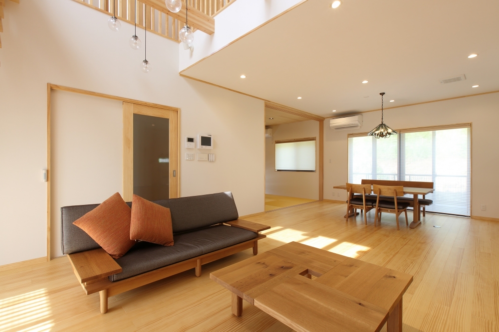 和モダン住宅の開放的なLDK空間。無垢フローリングと木製家具で統一されたナチュラルなインテリアに、吹き抜けからの自然光がやわらかく差し込む設計。リビングとダイニング、畳スペースが緩やかにつながり、動線と視線の広がりを確保。奈良の注文住宅における、ホテルライクで上質な暮らしを実現する快適な住まいの施工事例。