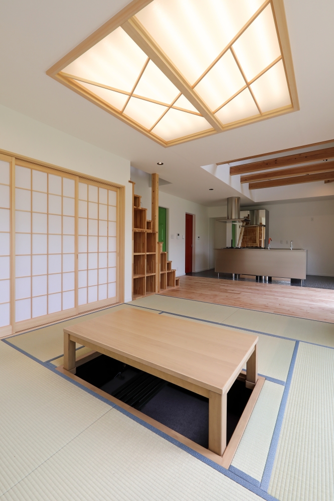 掘りごたつを中心に据えた畳リビングと、吹抜けLDKがゆるやかにつながる和モダン住宅のインテリア空間。障子越しのやわらかな光、無垢材の質感、木製格子収納が日本的な落ち着きを演出しながら、奥にはステンレス製アイランドキッチンを配置し、ホテルライクな洗練を融合。家族が自然と集まり、心地よい時間を共有できる、和モダンの家・注文住宅・自然素材の家・デザイナーズ住宅を求める方へ向けた建築家住宅の設計事例。