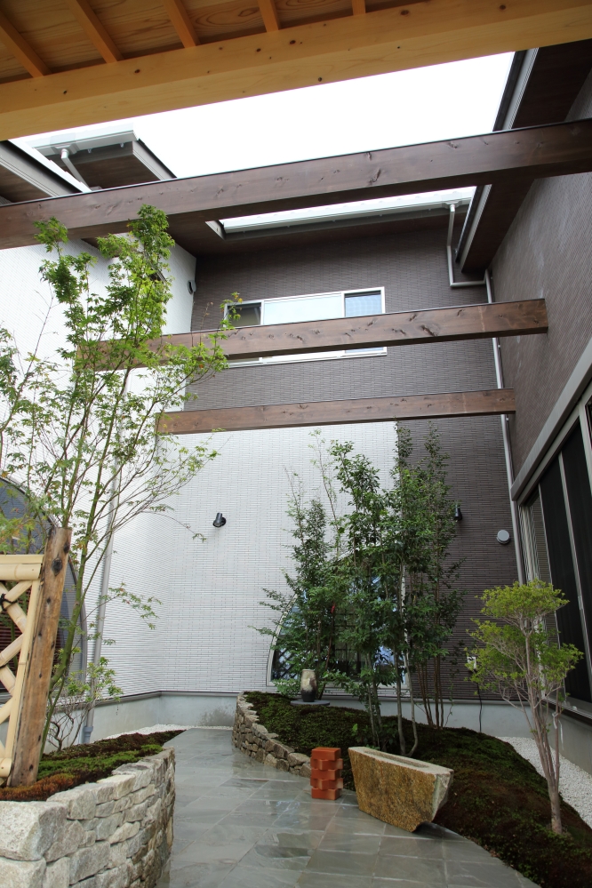 奈良県の建築家設計による高級和モダン住宅の中庭吹抜け空間。 木梁と開口部から自然光を取り込み、植栽と石積みの庭が調和した回遊動線を持つプライベート中庭の注文住宅デザイン。