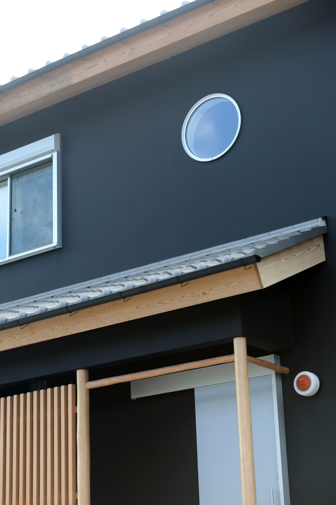 黒壁の外観に木格子と深い軒を組み合わせ、日本建築の美意識を現代的に昇華した和モダン住宅の外観デザイン。丸窓が静かな個性を添え、角地に建つ住まいとして街並みに凛とした存在感を生み出している。無垢材の軒天や縦格子が、旅館のような落ち着きと上質感を演出し、ホテルライクな暮らしを求める家づくり検討者に向けた設計事例。和風住宅・純和風の家・黒い外観の家・デザイナーズ住宅・高級和モダン住宅に関心のある人へ向け、光・陰影・素材感・余白の美しさを丁寧に整えた注文住宅。