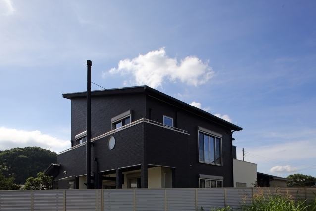 和モダン住宅の外観デザイン。ブラックの外壁とフラットな屋根形状が水平ラインを強調し、シンプルで重厚感のある佇まいを形成。開口部の配置とバルコニーの構成によりプライバシーと開放性を両立し、落ち着きと品格を備えたホテルライクな注文住宅。