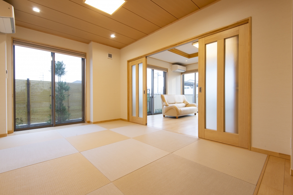 奈良県のやまぐち建築設計室が設計した和モダン住宅の和室空間。市松敷きの畳と自然素材の木質感が調和し、引き戸を開放することでリビングと一体化する可変性のある間取り。大開口窓からは坪庭と外構の竹垣が見え、採光・通風・視線の抜けを確保した設計。高級注文住宅における和室の現代的活用と空間設計の実例。