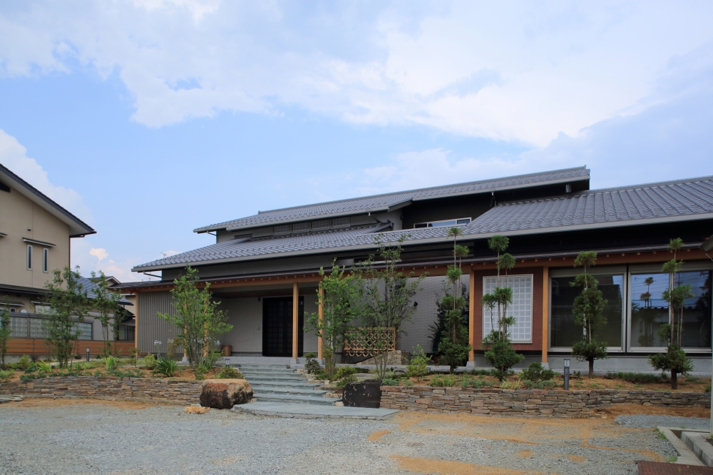 奈良県の建築家設計による高級和モダン住宅の全景外観。 瓦屋根と深い軒、木の質感と石積みの外構、植栽が調和し、落ち着きと品格を兼ね備えた注文住宅の庭とアプローチデザイン。