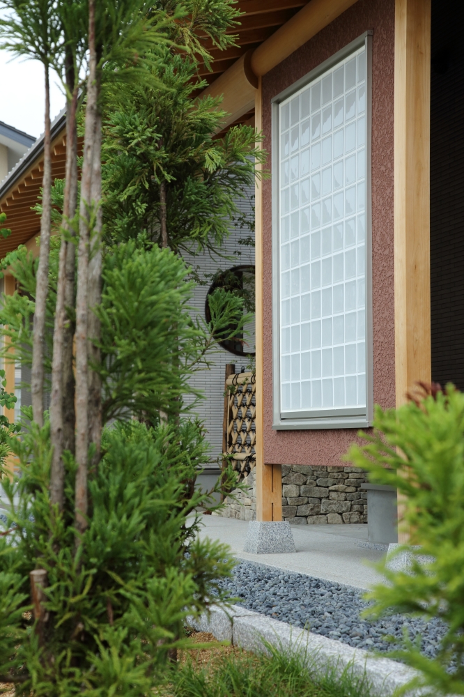 奈良県の建築家設計による高級和モダン住宅の外観ディテール。 無垢の柱と深い軒、格子デザインの窓と石積み基壇、植栽が調和し、プライバシーと美しさを両立した注文住宅の外構設計。