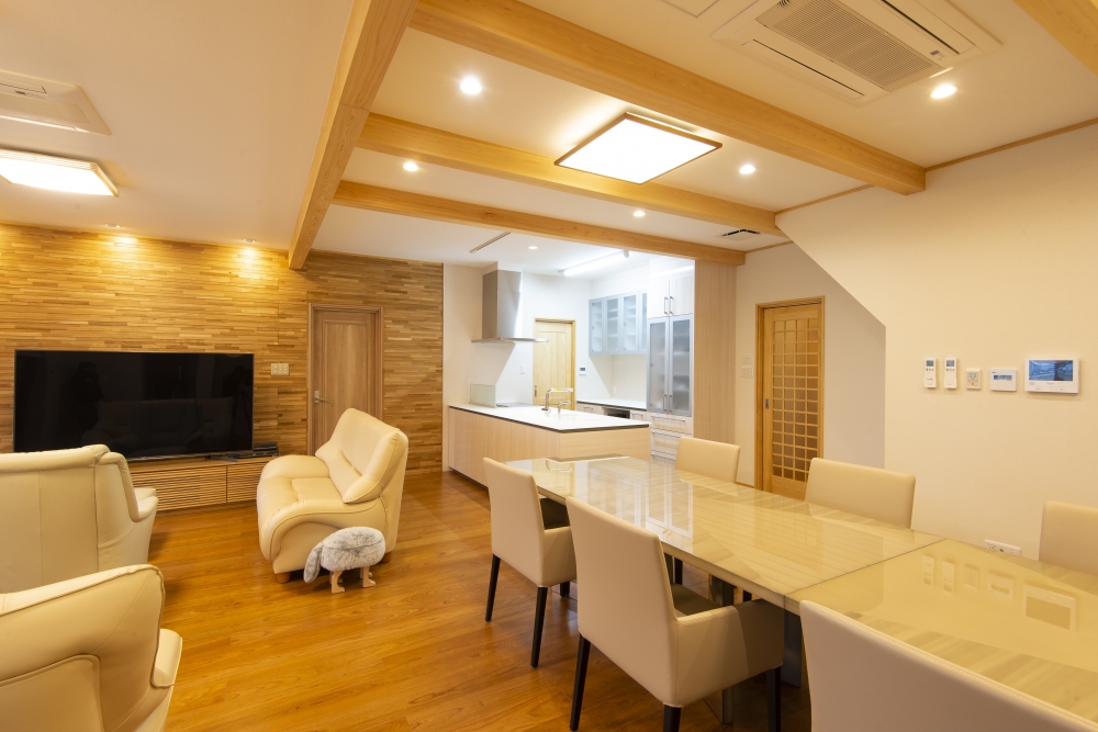 奈良県のやまぐち建築設計室が設計した和モダン住宅のLDK空間。無垢材の梁と床が織りなす温かみあるインテリアに、木質アクセントウォールと大型テレビを配置したリビング、対面式アイランドキッチンと長尺ダイニングを一体化。回遊動線と視線の抜けを意識した設計で、家事効率と居住性を高めた高級注文住宅の実例。